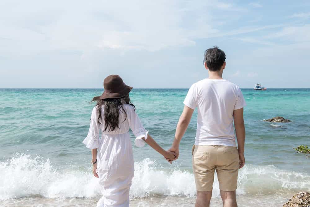 A couple in white holding hands on a beach in Thailand